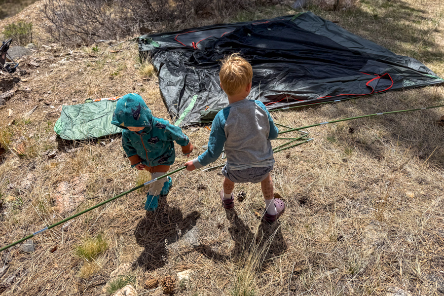 Two children helping assemble the Kelty Wireless 6 tent poles during setup in a dry grassy campsite.