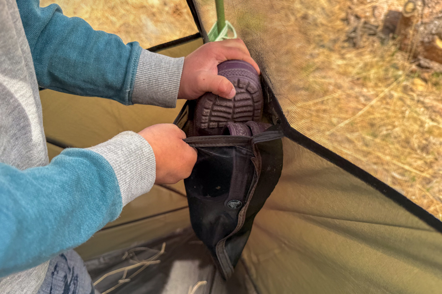 Close-up of a child placing shoes into one of the Kelty Wireless 6 tent's interior corner storage pockets.