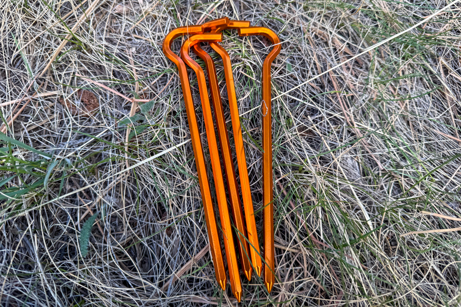 A set of orange aluminum stakes included with the Kelty Wireless 6 tent laid out on dry grass.