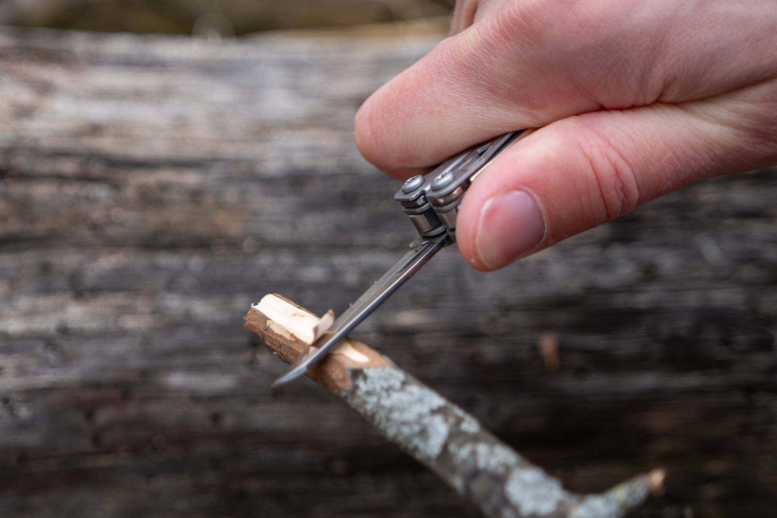 A hand holds multitool and whittles the end of a stick