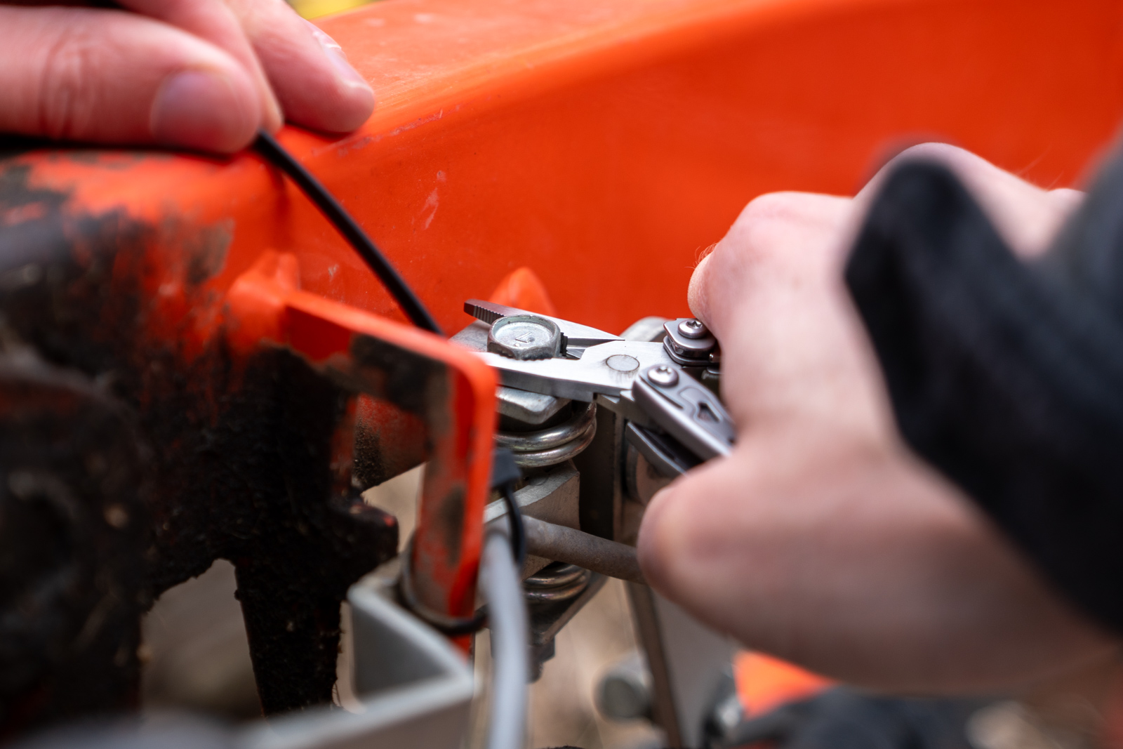 A hand holds a multi tool pliers grabbing onto a bolt on a red machine