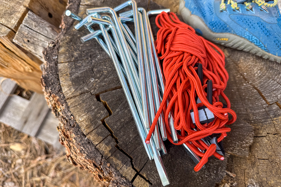 Close-up of the REI Base Camp 6 tent's stakes and bundled guylines laid out on a weathered tree stump.
