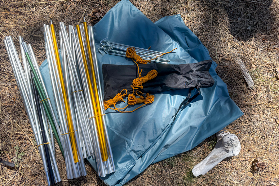 The REI Westard 6 tent's pole set, stakes, guylines, and tent body laid out on the ground before pitching.