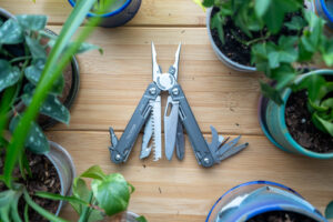 A multi tool with its implements spread wide sits on a desk surrounded by plants