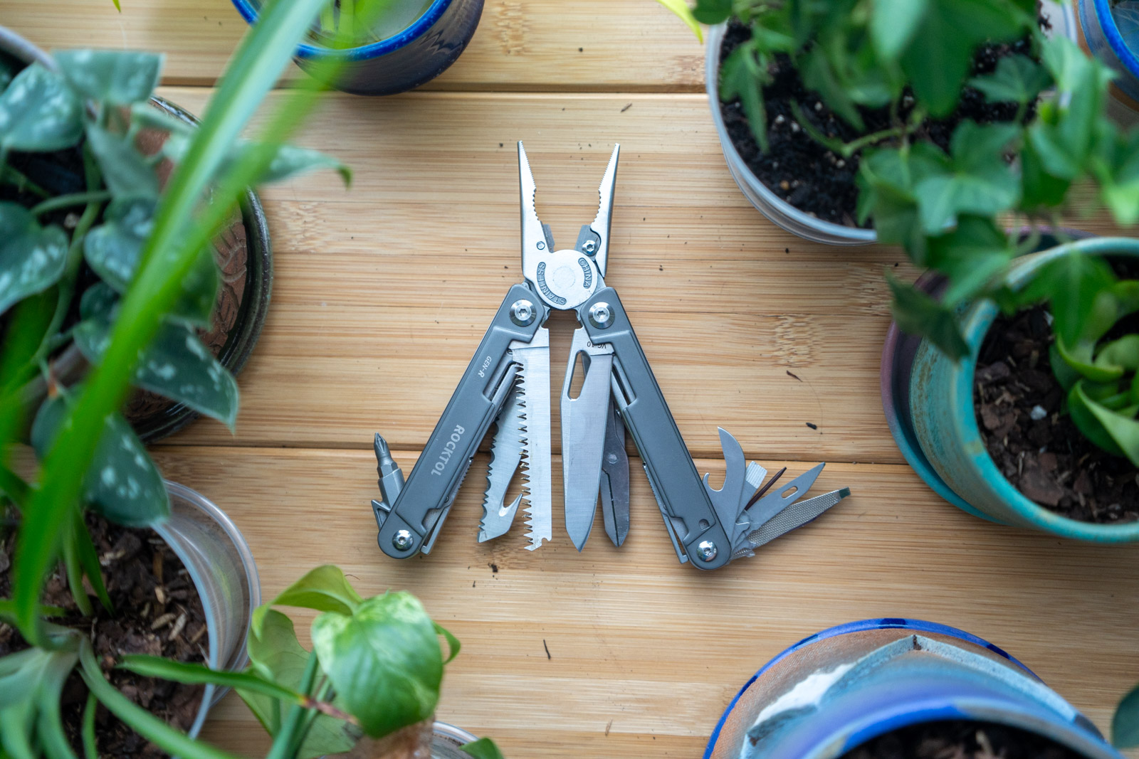 A multi tool with its implements spread wide sits on a desk surrounded by plants