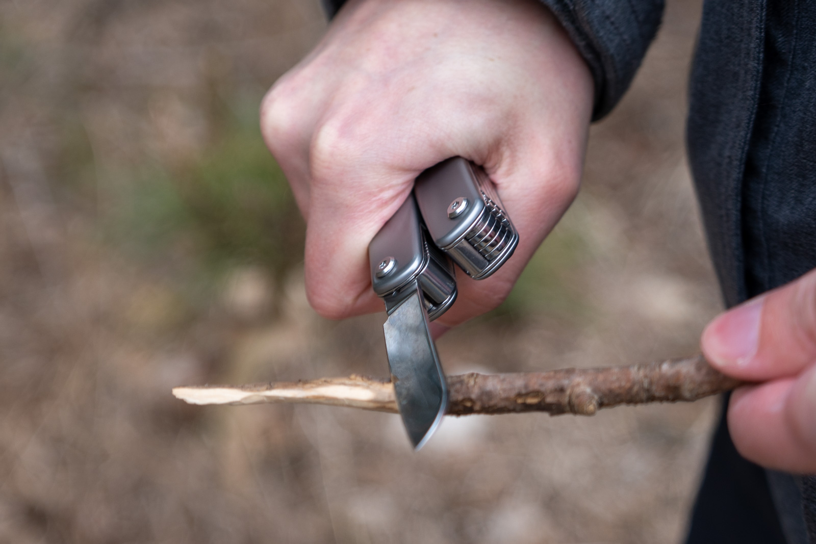 A hand uses a multi tool to cut a branch