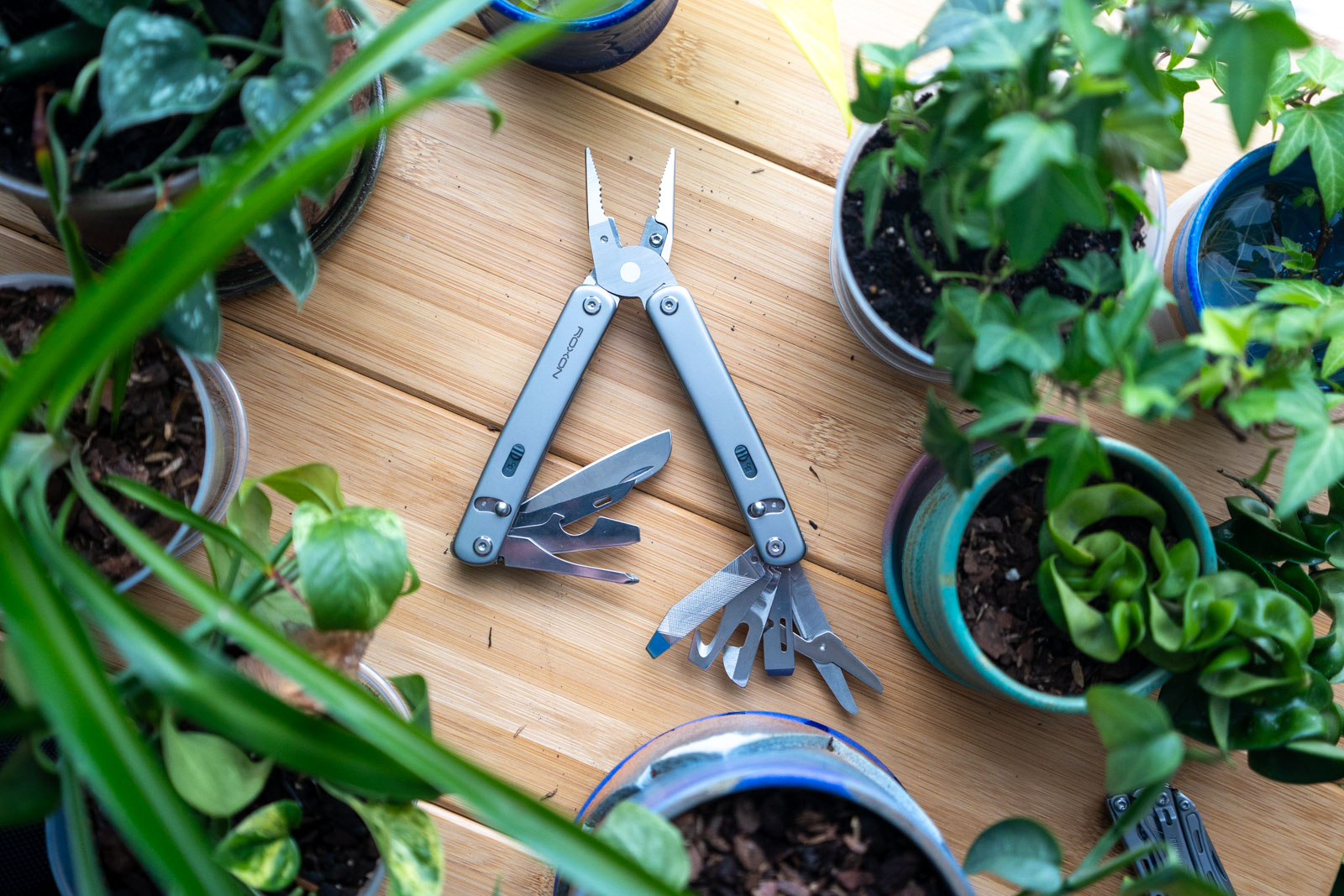 A multi tool with its implements spread sits on a table surrounded by plants