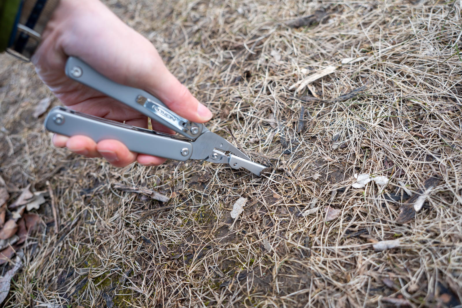A hand uses a multi tool to pull a tent stake out of the ground