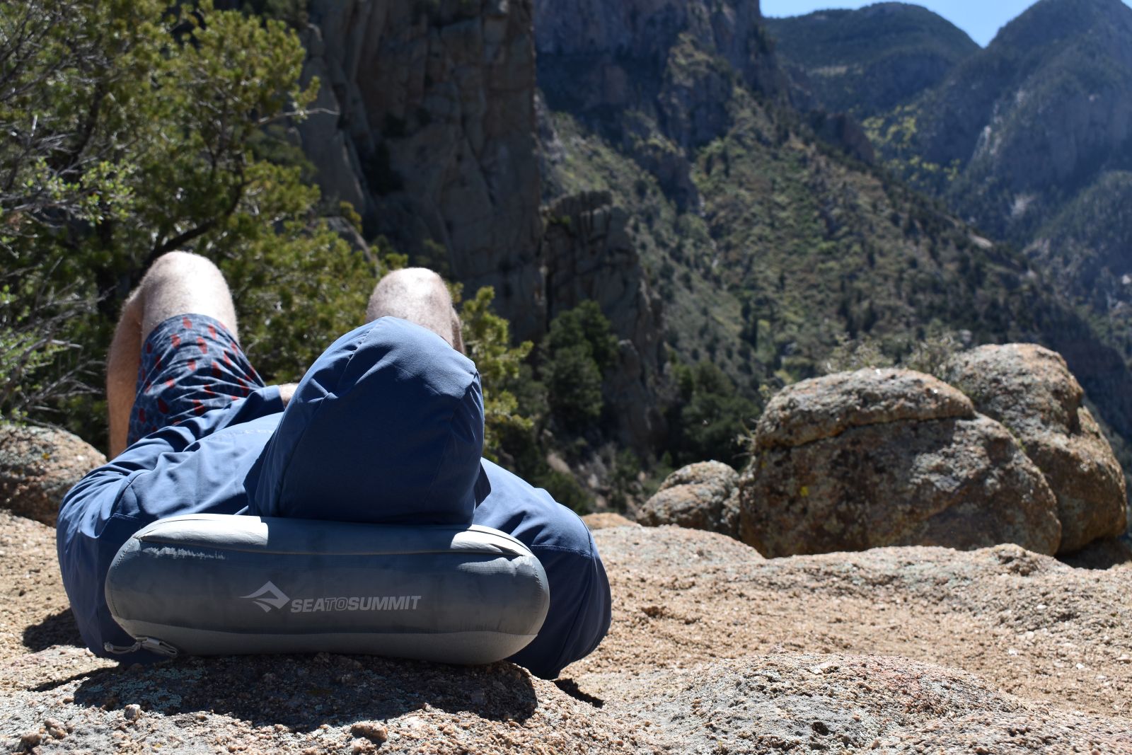 A hiker rests on the Aeros Down Pillow on a mountain saddle.