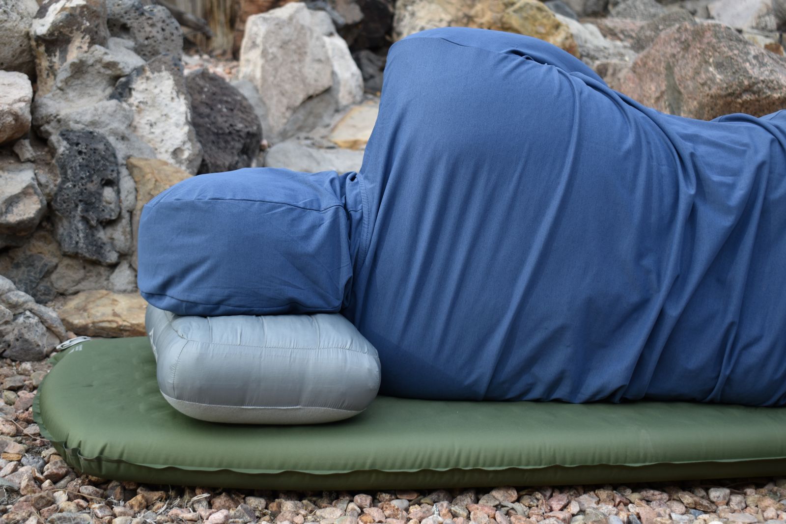 A person faces away while lying on the Sea to Summit Aeros Down pillow on top of a sleeping pad.