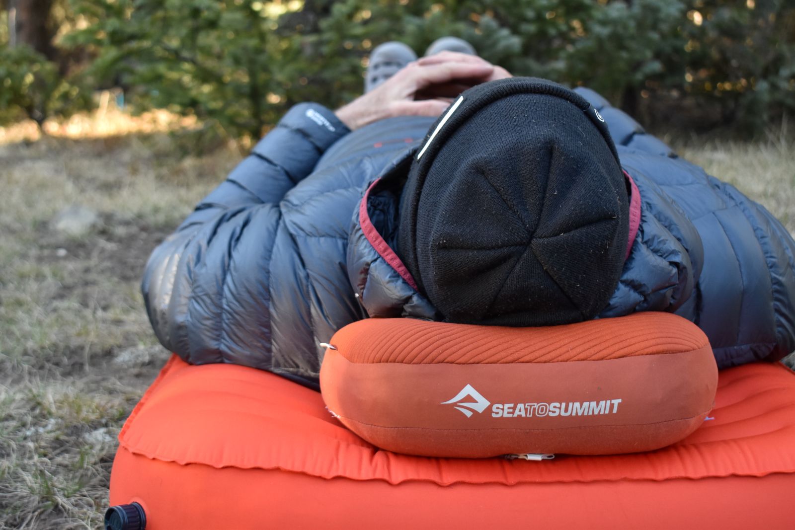 Close up of the Aeros Premium pillow under our tester's head while laying on a sleeping pad in the wilderness.