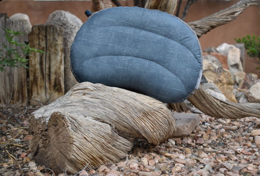 A blue-gray Therm-a-Rest Air Head Down pillow placed on a piece of driftwood.