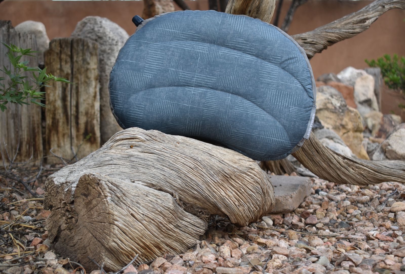 A blue-gray Therm-a-Rest Air Head Down pillow placed on a piece of driftwood.