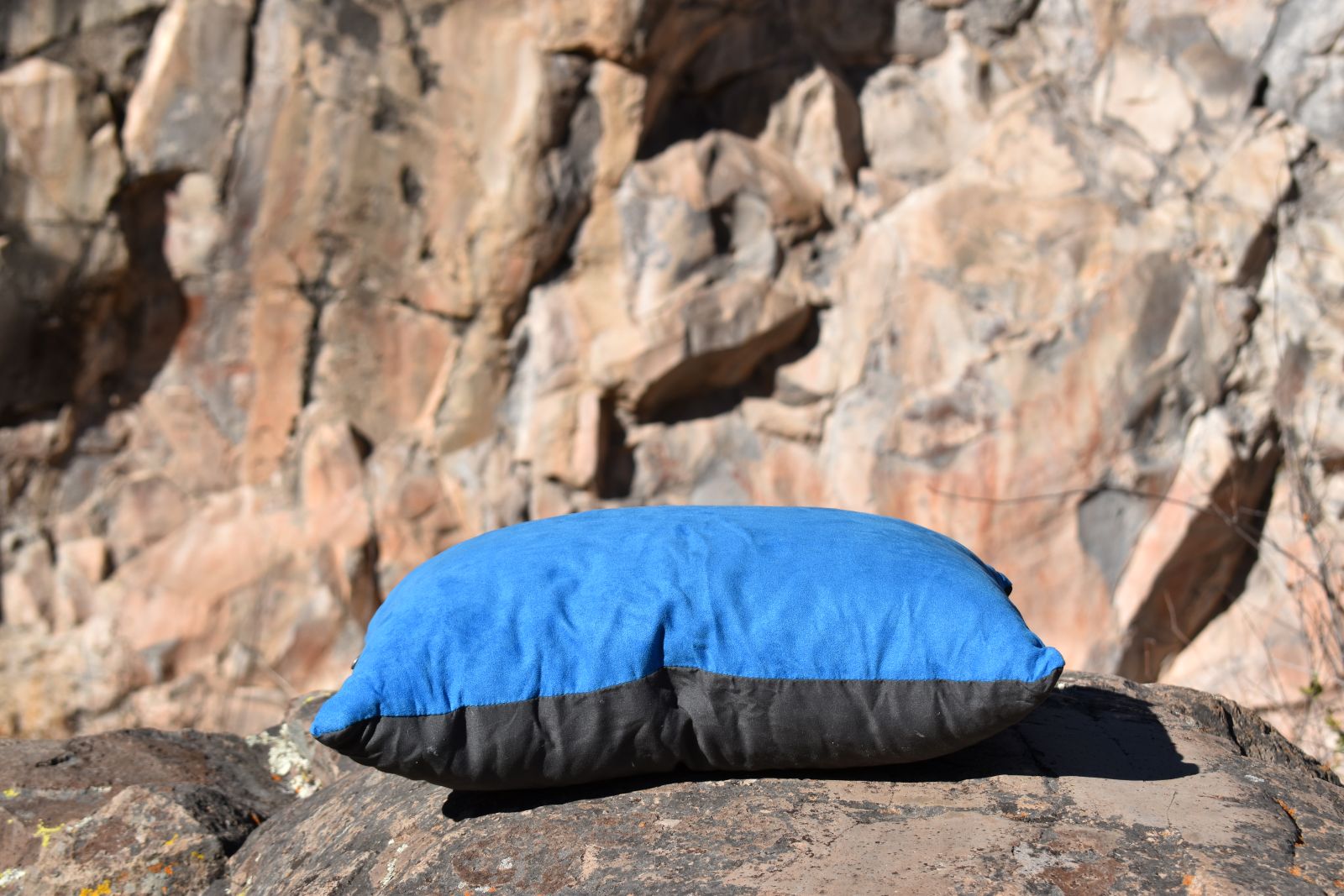A blue and gray pillow rests on desert rocks with faint pictographs on the rock face in the background.