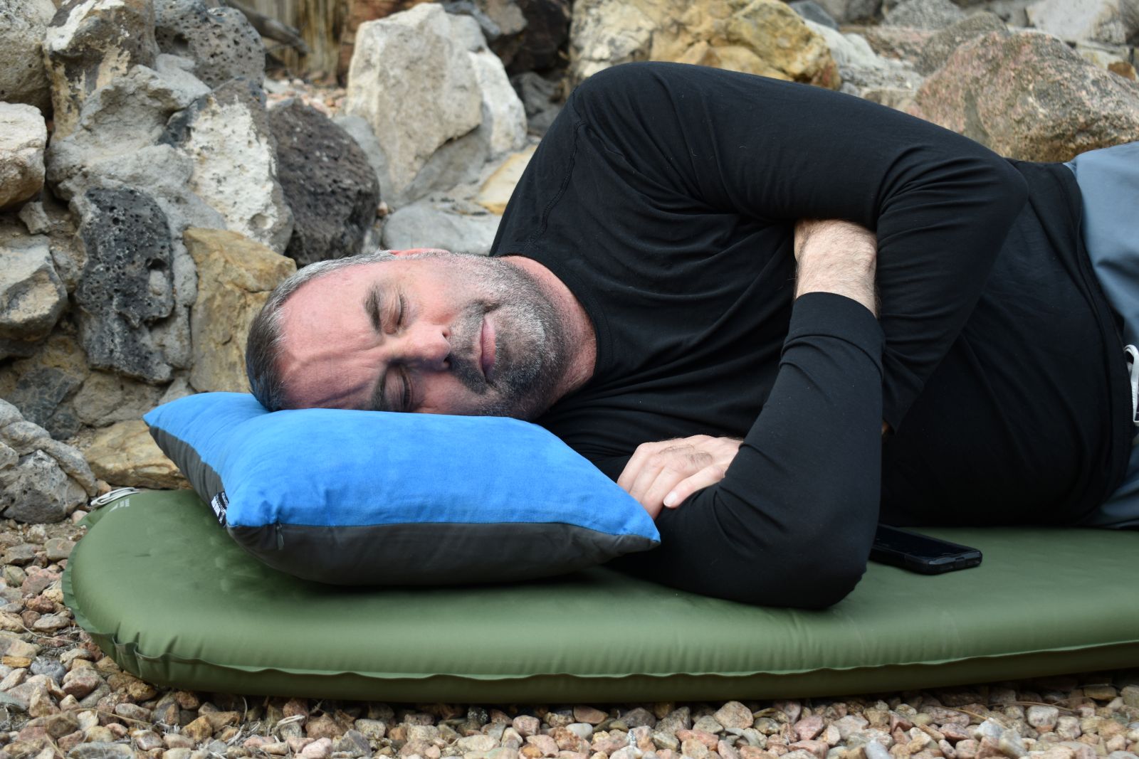 A tester lies on his side with his head resting on a blue Wise Owl Snoozy pillow.