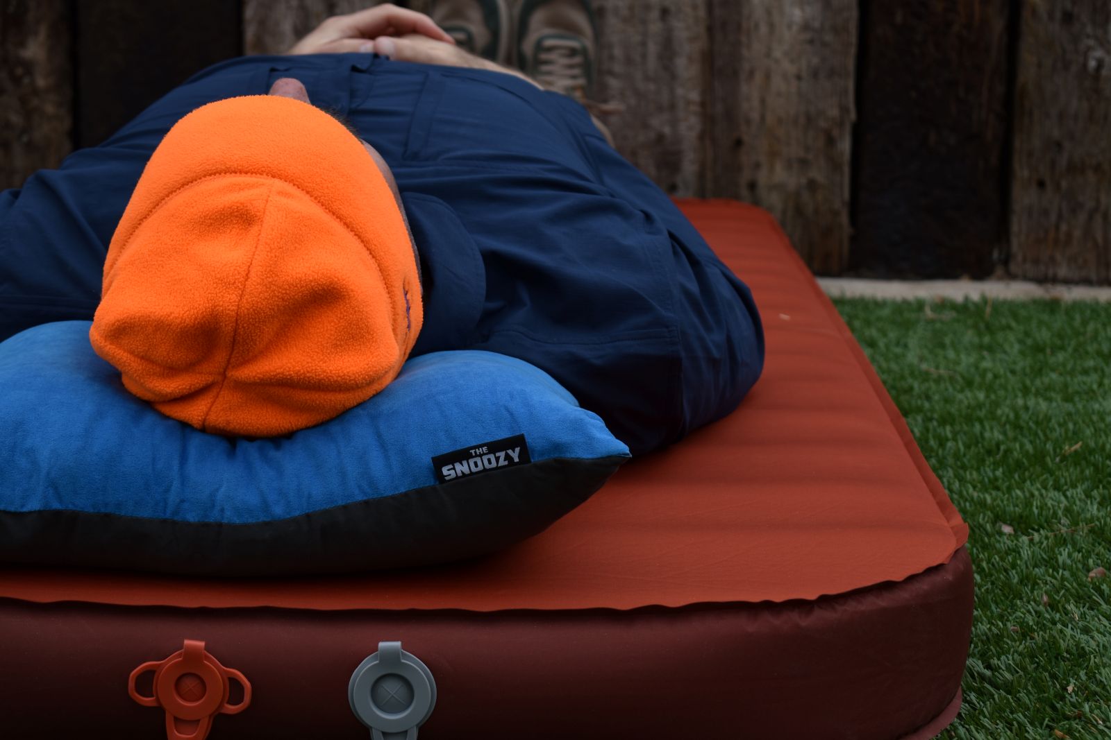 A hiker in an orange hat lays on a blue Wise Owl Snoozy camping pillow.
