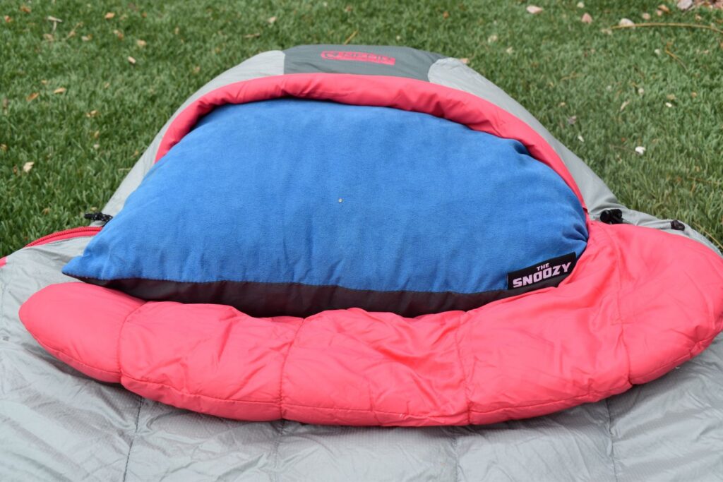 A blue camping pillow lies in the hood of a women's NEMO Disco sleeping bag.