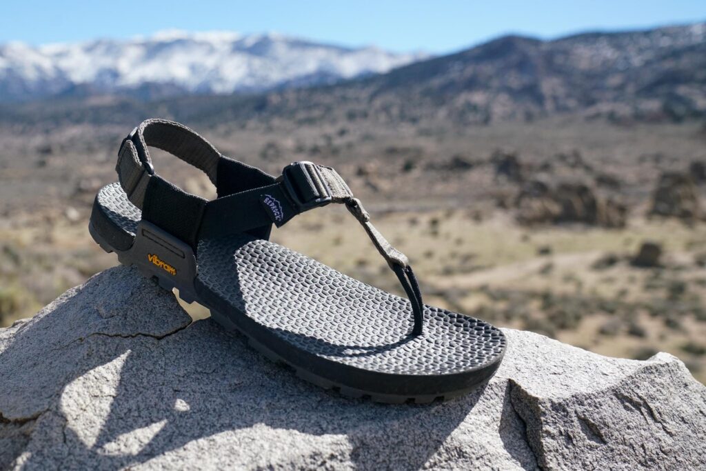 A close up of a single sandal sitting on a rock with mountains in the background.