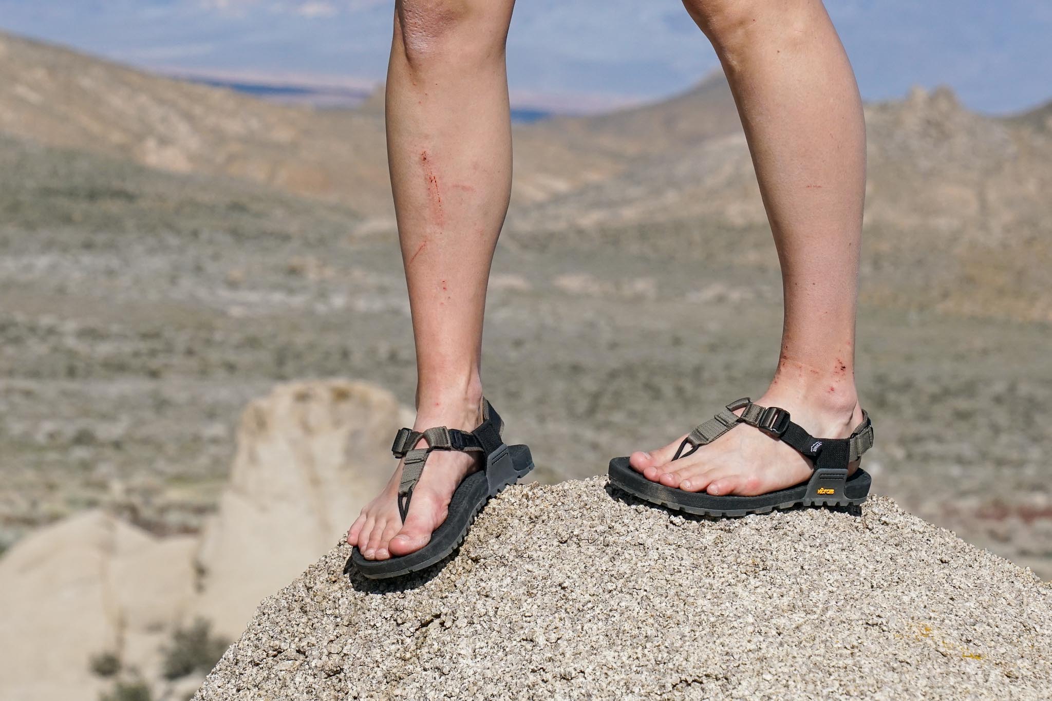 A close up of a person's feet wearing sandals standing on a rock.