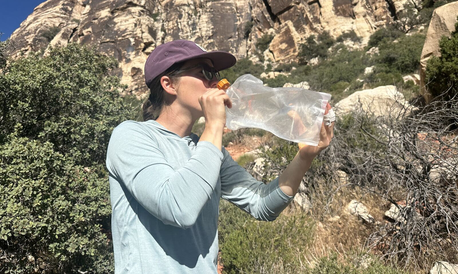 Un excursionista en un entorno desértico bebe de una bolsa de hidratación sin manguera.