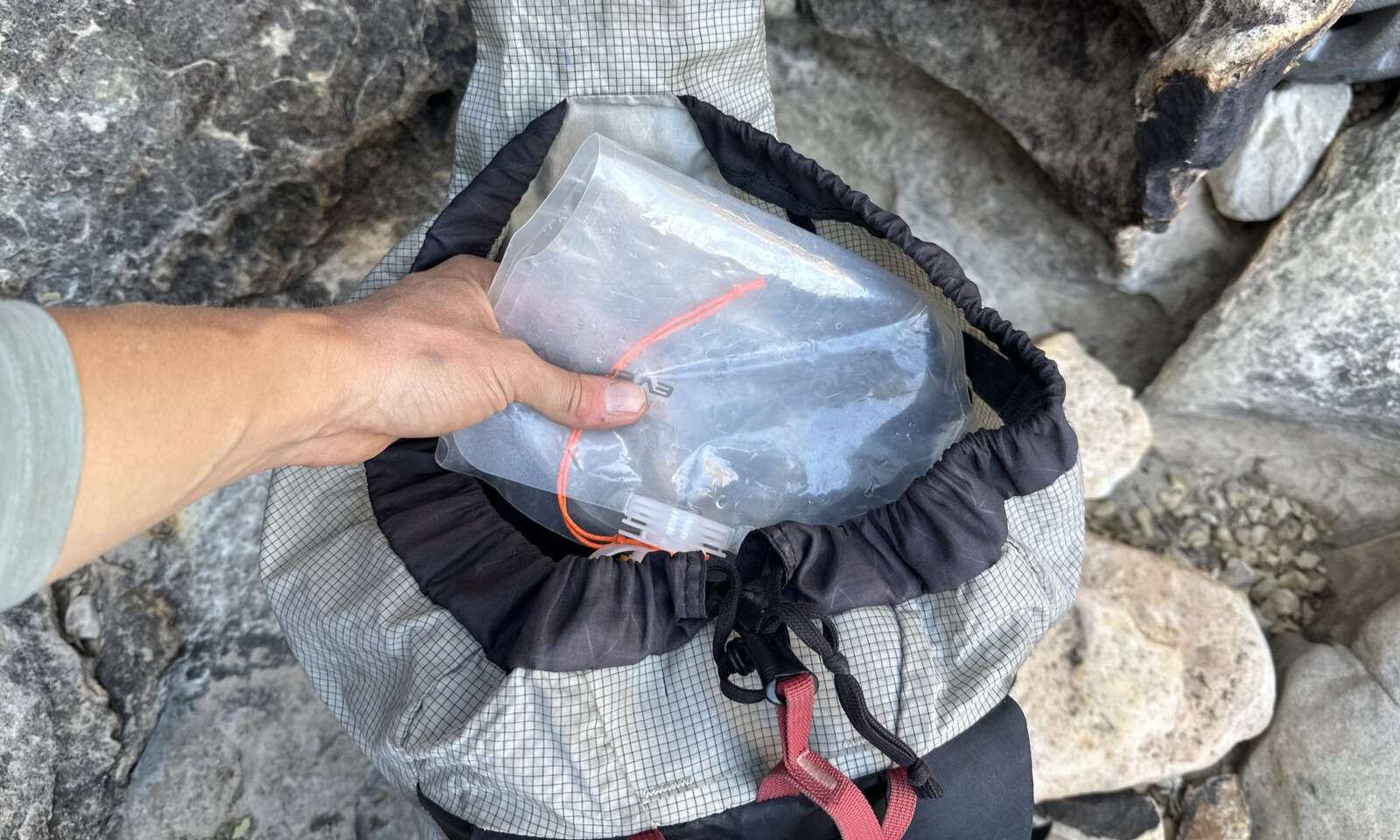 Un excursionista coloca una bolsa de agua vacía y enrollada en la parte superior de una mochila llena.