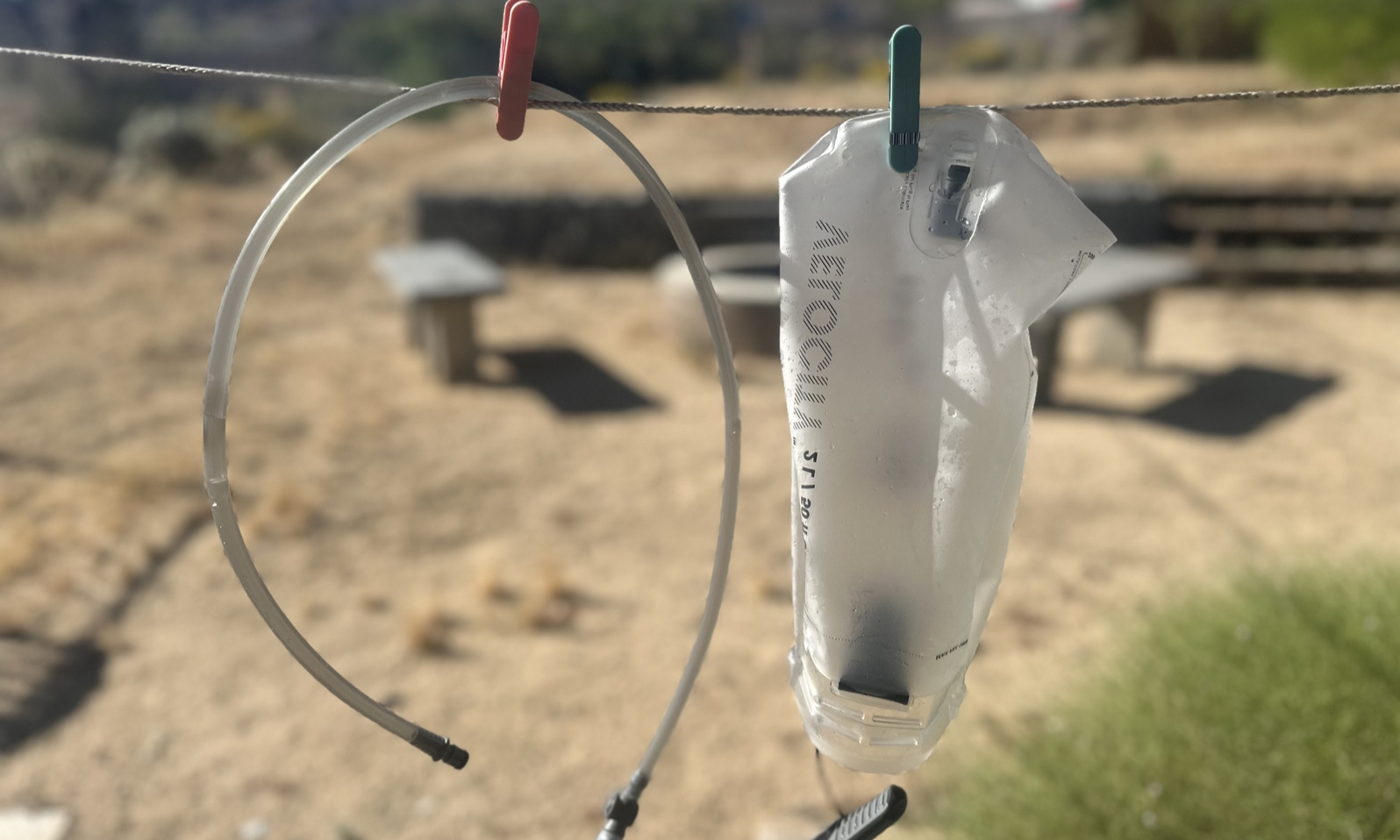 A hydration bladder and hose are hung up to dry on a clothesline outside