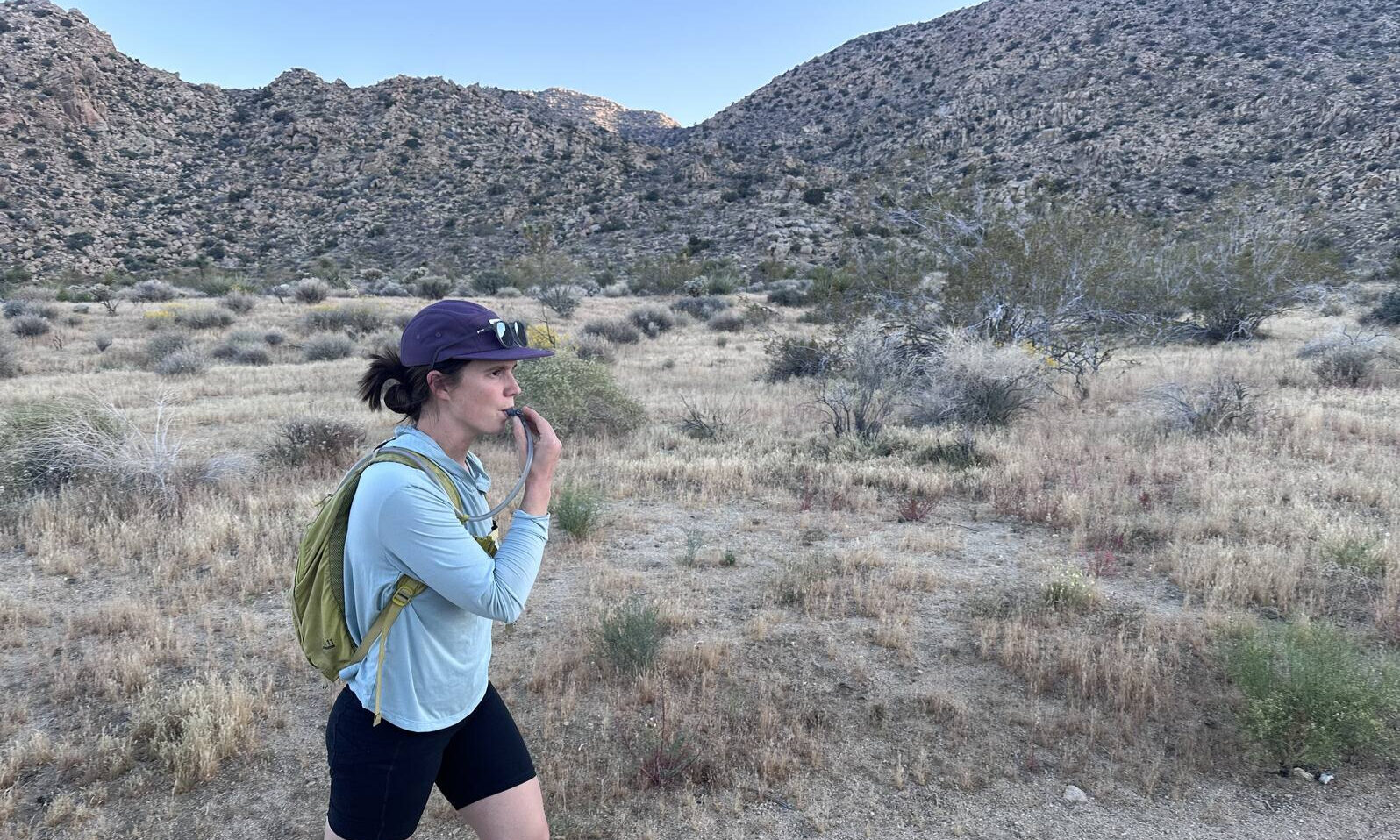 A hiker drinks from a hydration hose while hiking in the desert.