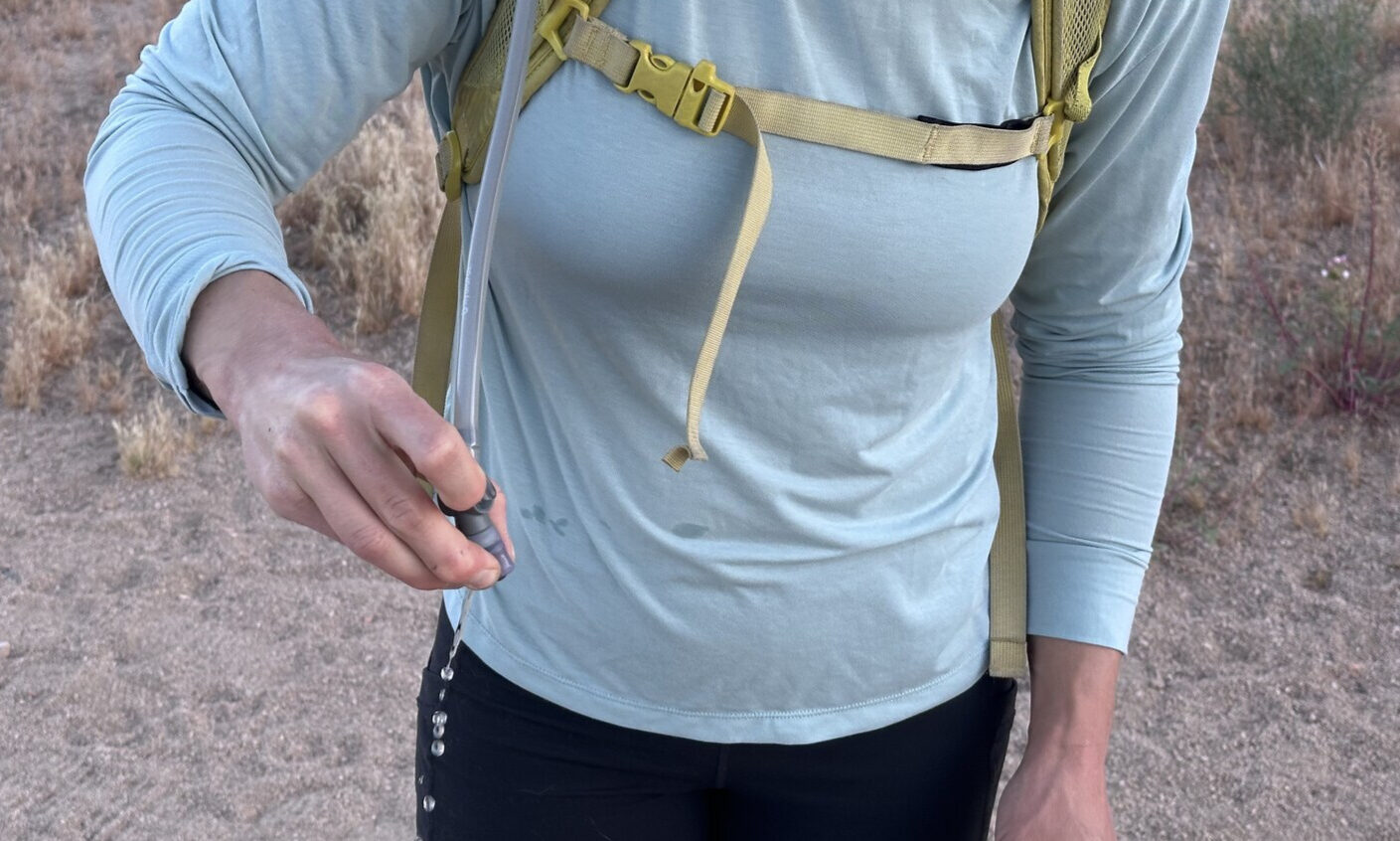 Close up of a hiker pinching the bite valve on a hydration hose. Water droplets are coming out of the valve.