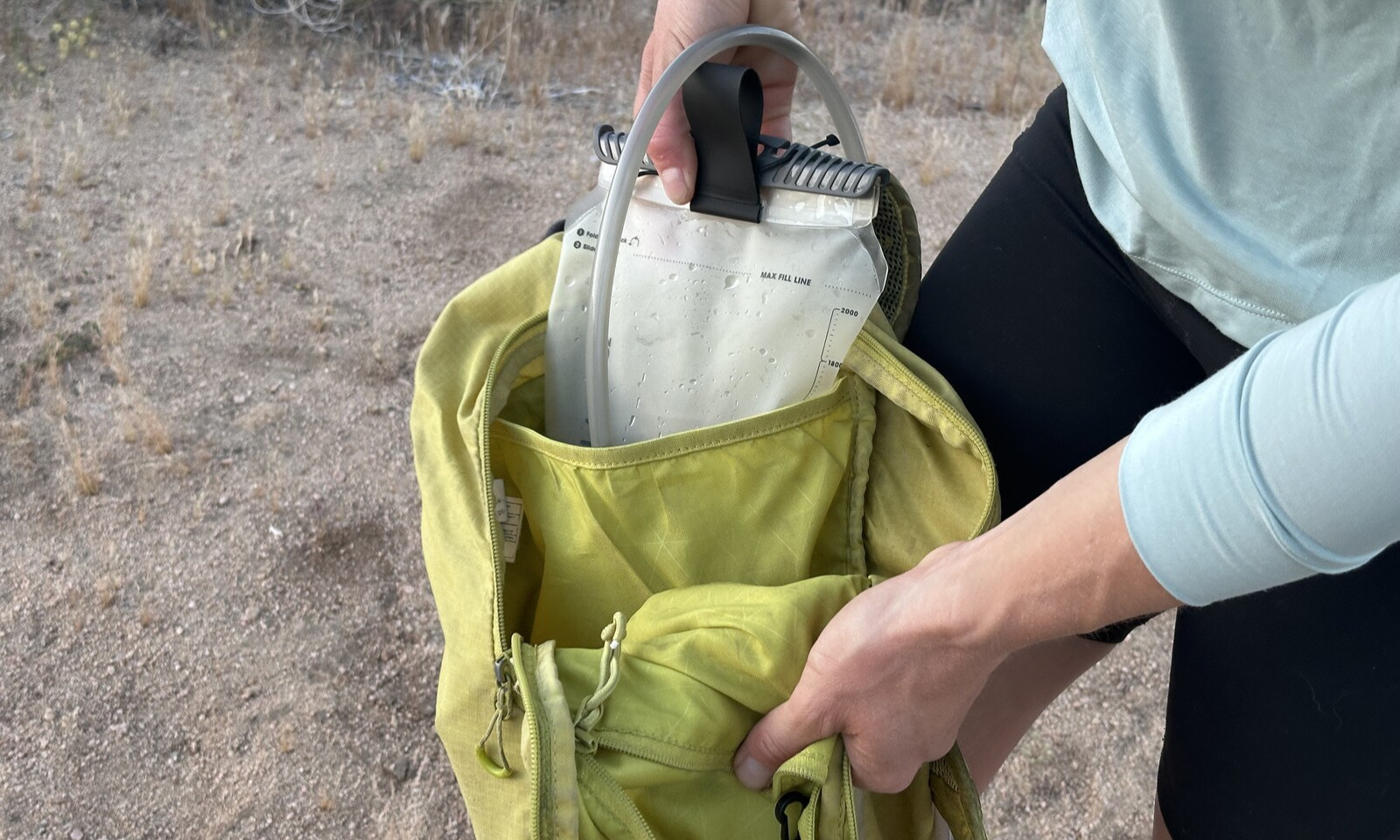Close up of a hiker loading a hydration bladder into the hydration sleeve of a small yellow backback