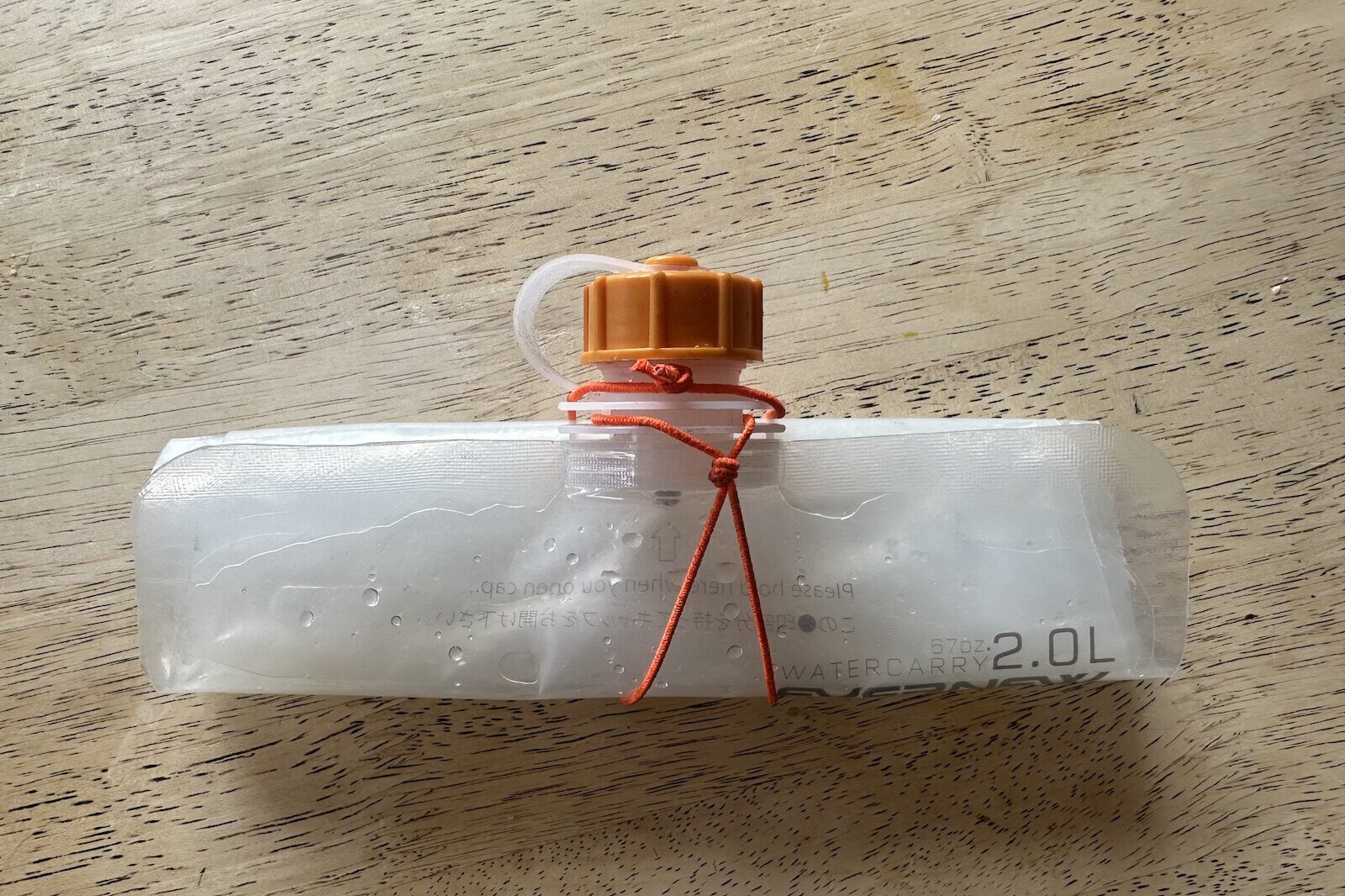 Una bolsa de hidratación está vacía y enrollada, asegurada con una pequeña cuerda elástica de color naranja.