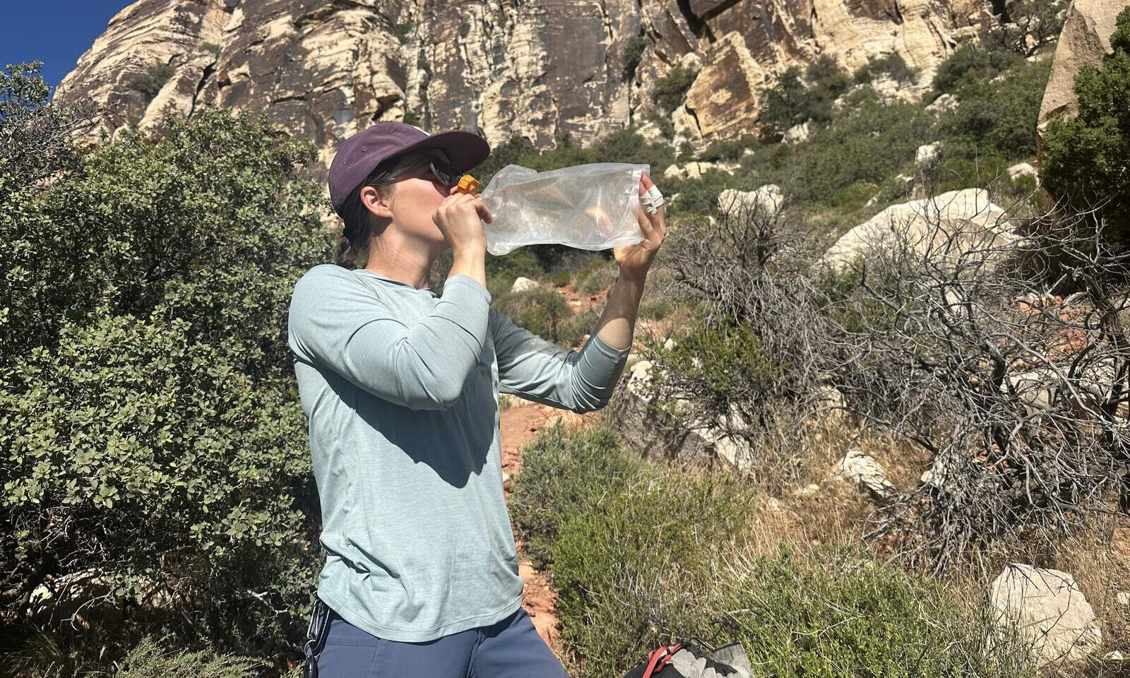 Un excursionista en un desierto sacando bebidas de una vejiga de hidratación sin manguera.