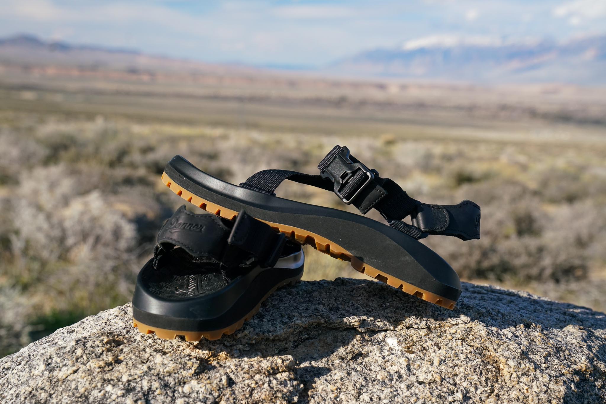 A close up of a pair of sandals sitting on a rock with mountains in the background.