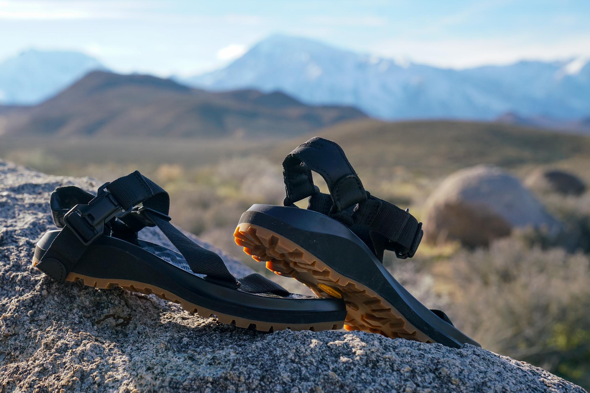 A close up of a pair of sandals sitting on a rock with mountains in the background.