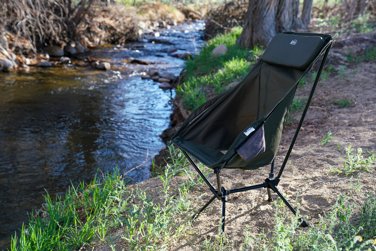 An empty scoop-seat camping chair sits next to a creek.