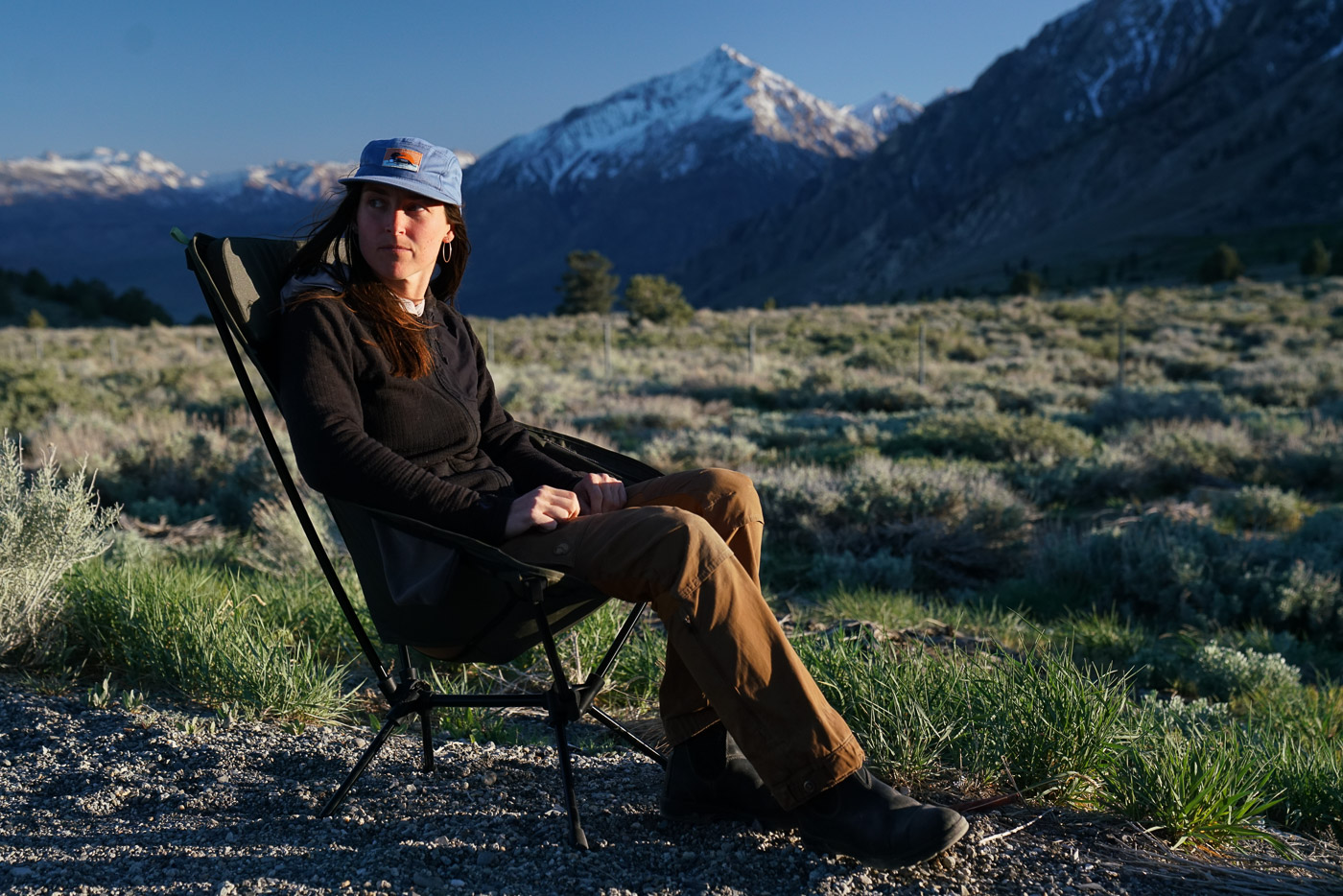 A person sits in a scoop-seat camping chair with mountains in the background.