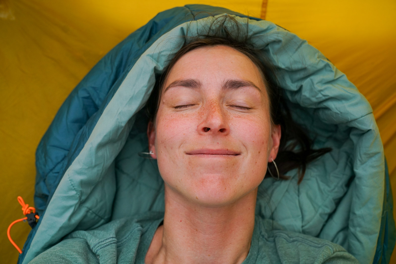 A close up of a person's face with a sleeping bag hood around their head.