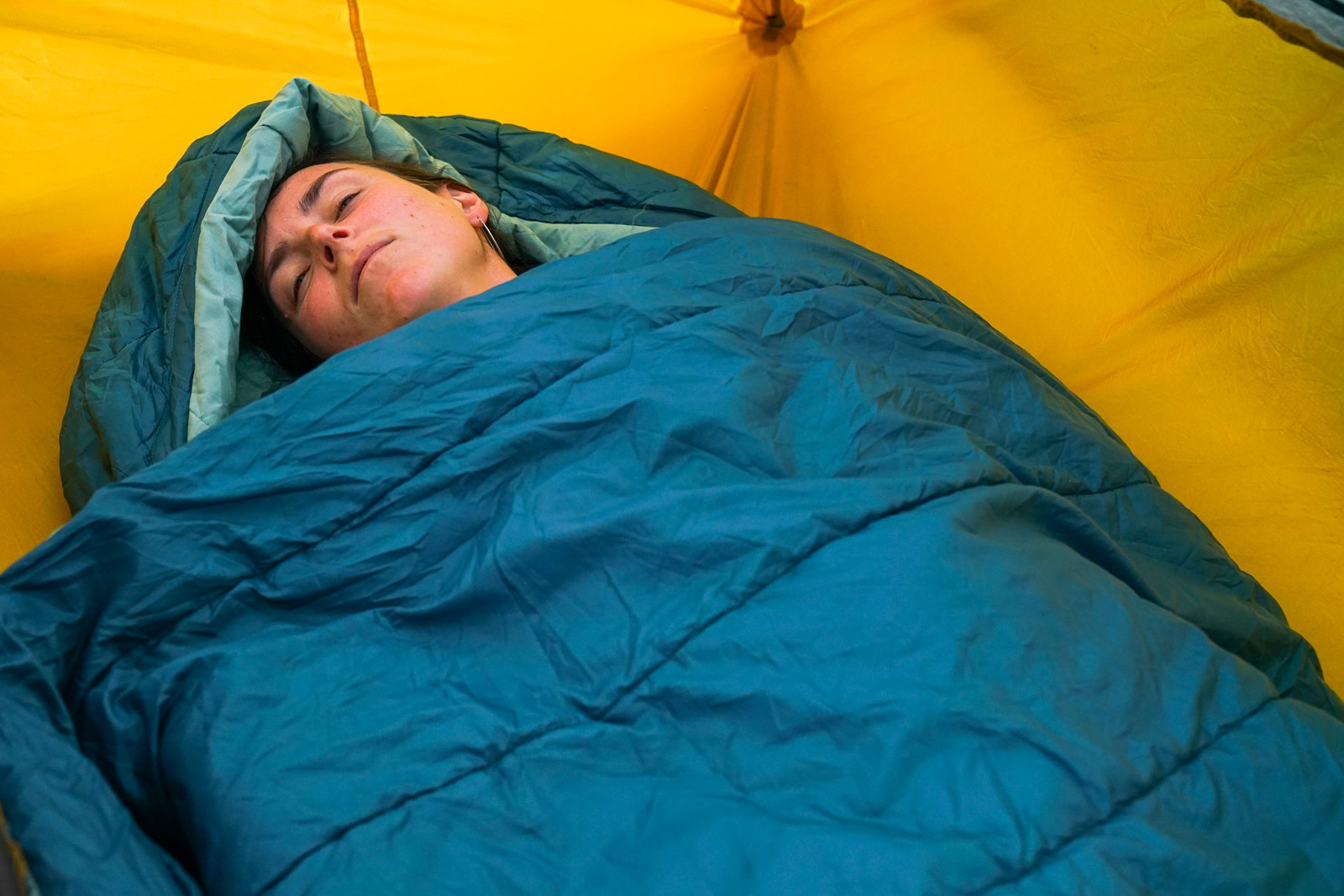 A close up of a sleeping person's face sticking out of a sleeping bag.