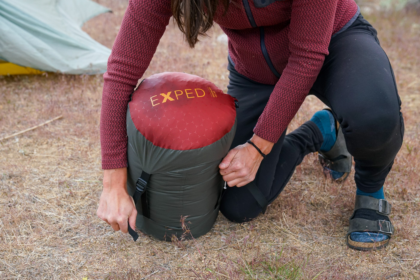 A person adjusts the straps on a sleeping bag compression sack.