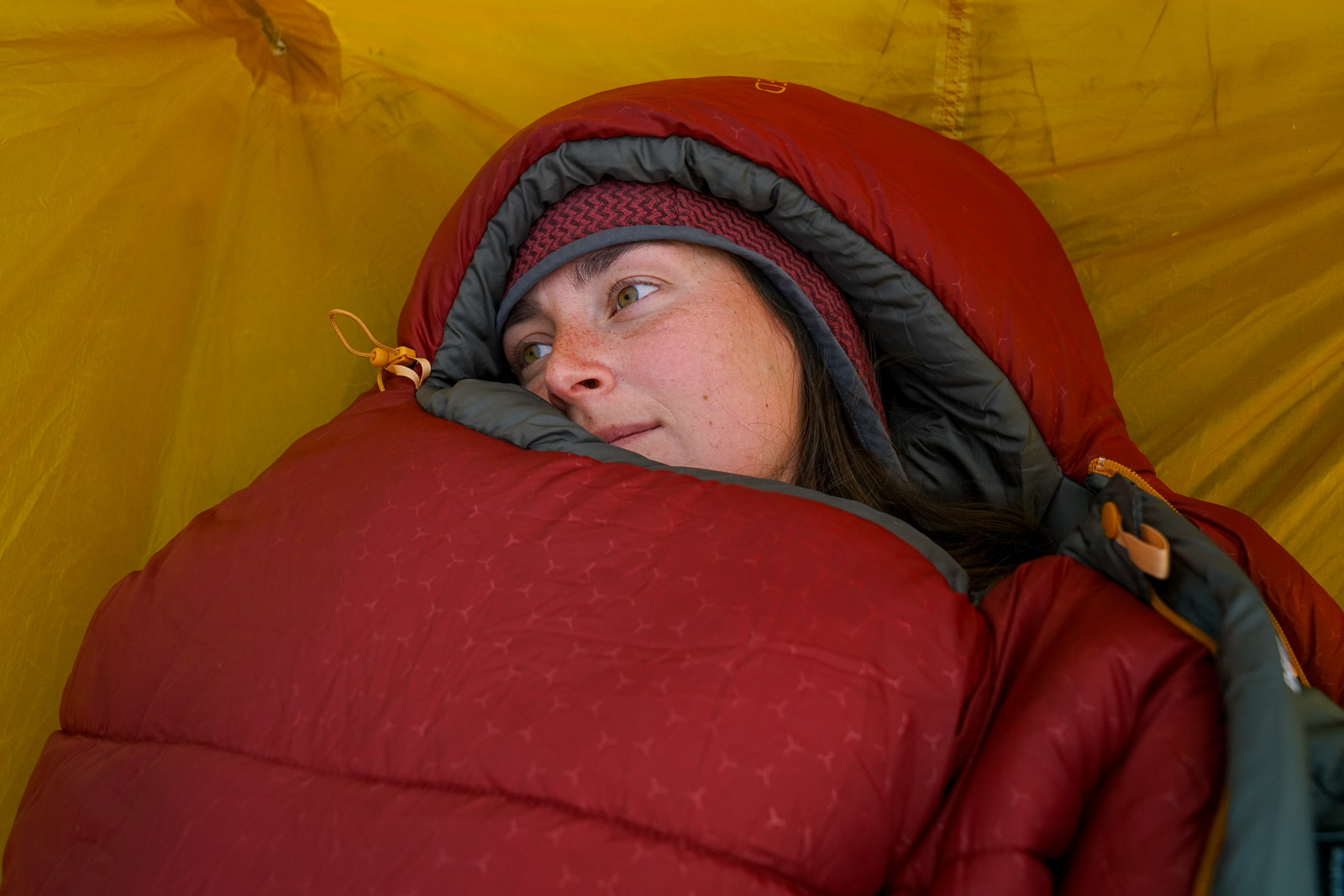 A close up of a person's face sticking out of a sleeping bag.