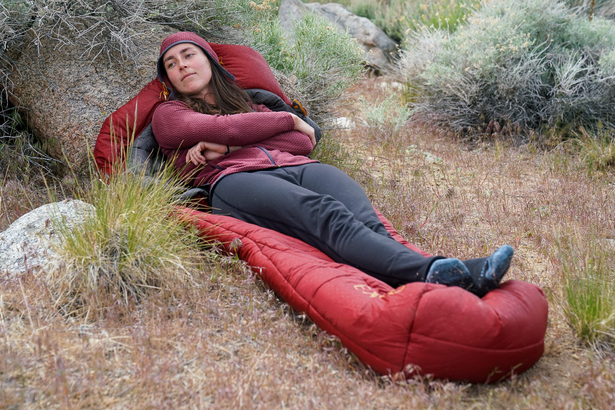 A person lays on top of a sleeping bag on the ground.