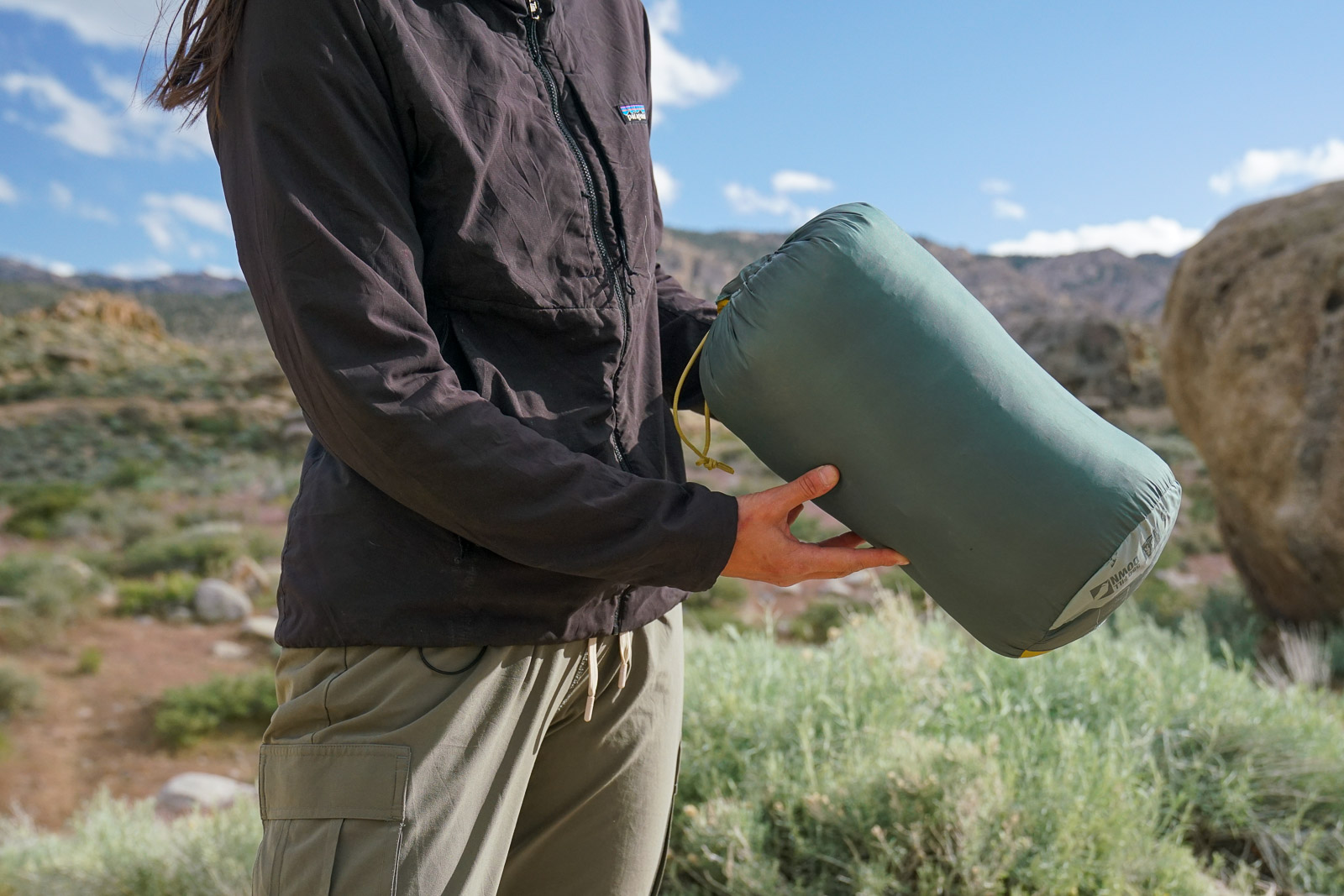 A close up of a person holding a sleeping bag in a stuff sack.