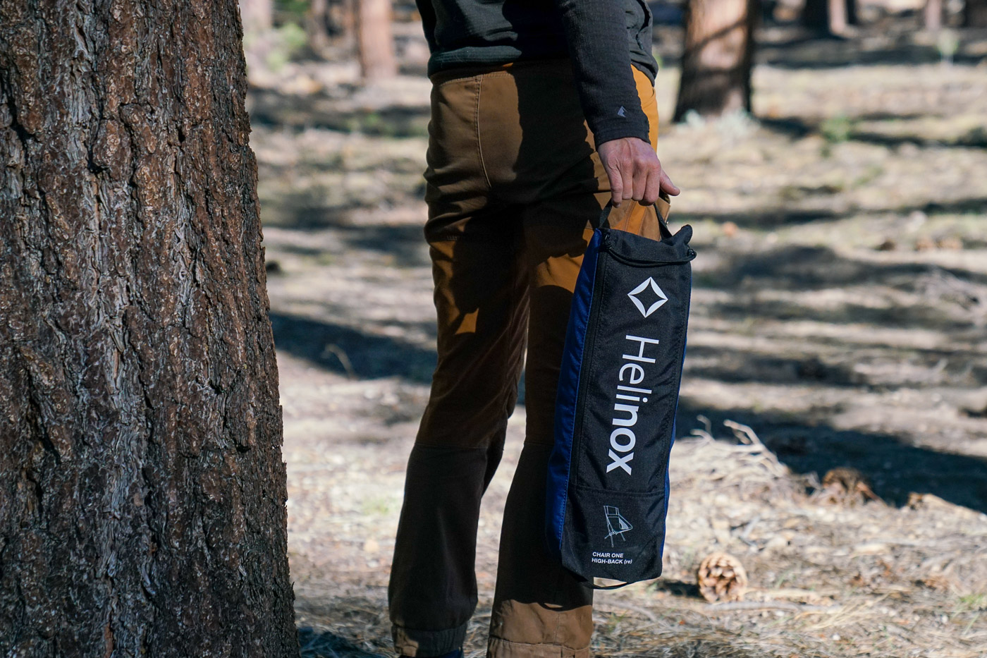 A close up of a person holding a camping chair packed into its carry case.