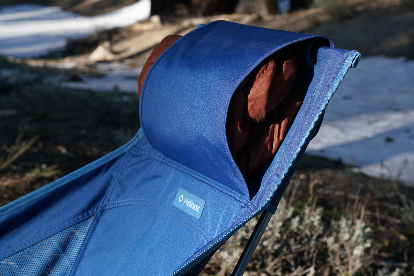 A close up of a jacket stuffed into the headrest sleeve of a camping chair.