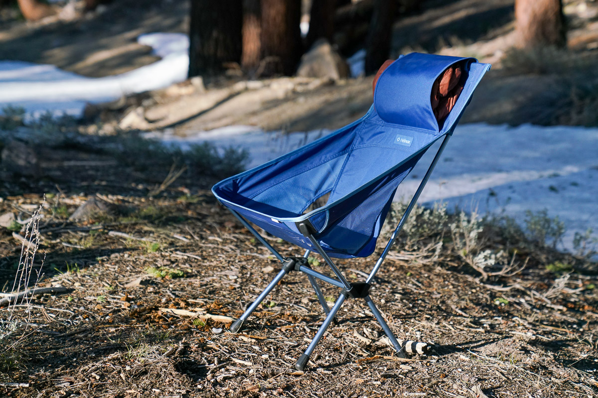 An empty scoop-seat camping chair sits in a forest with snow on the ground.