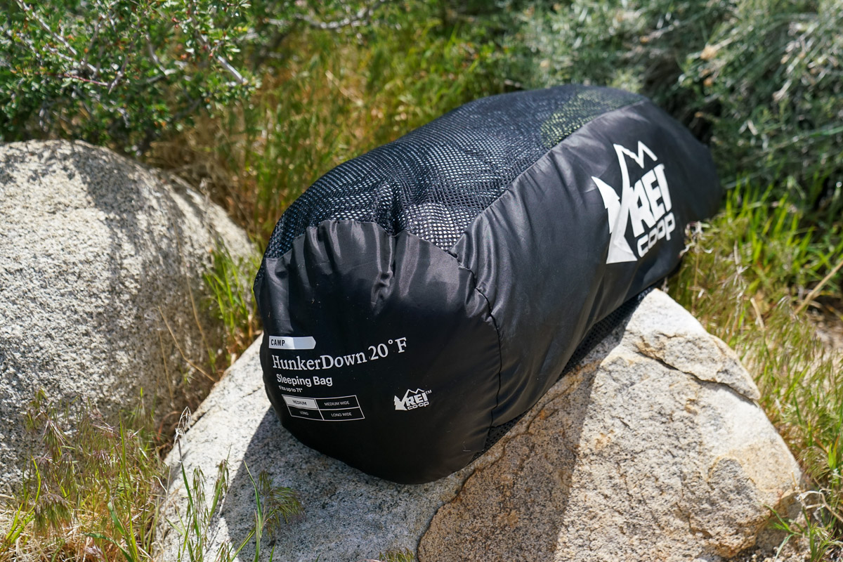 A close up of a sleeping bag stored in a mesh sack. The sack sits on a rock.