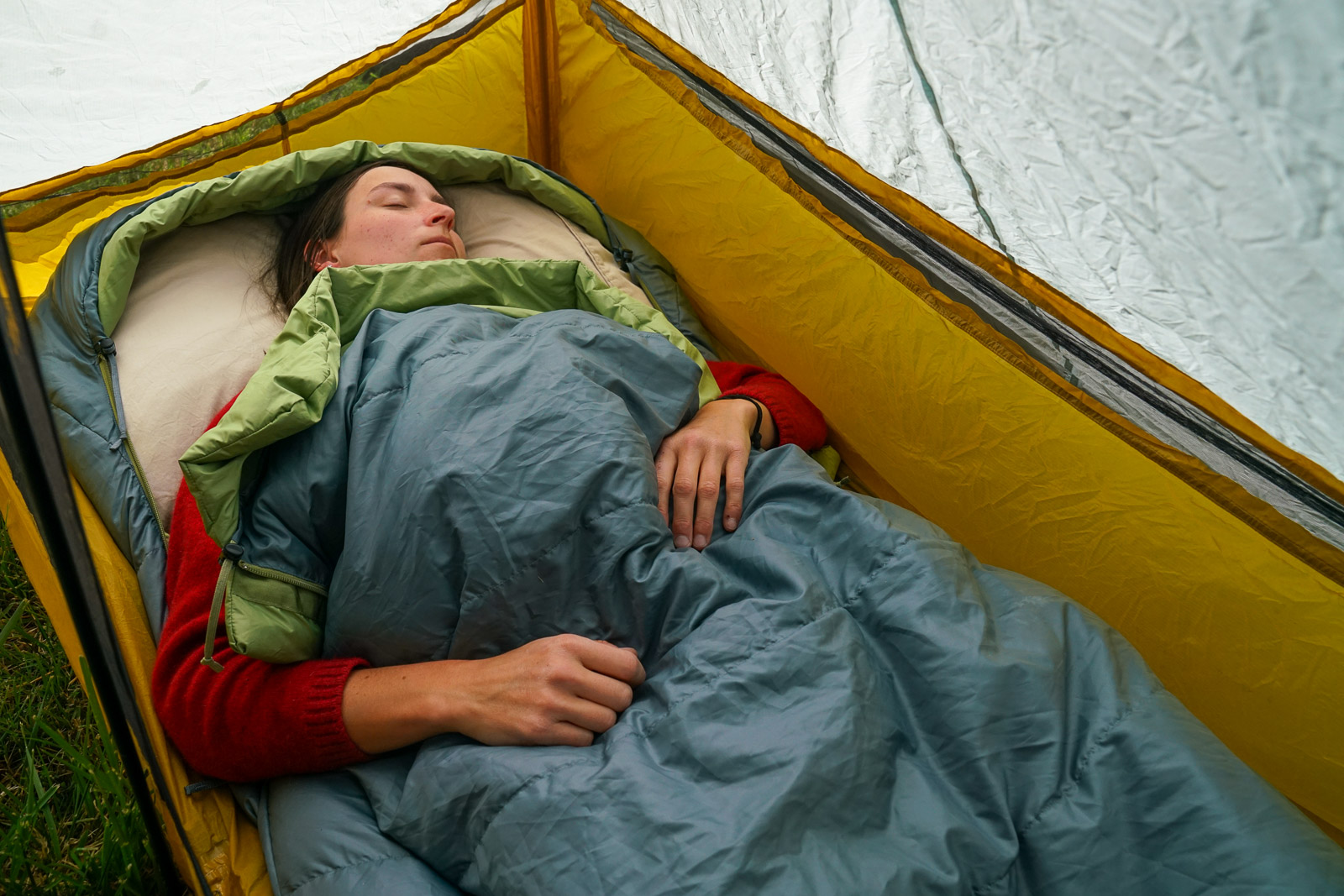 A person sleeps in a sleeping bag in a tent.
