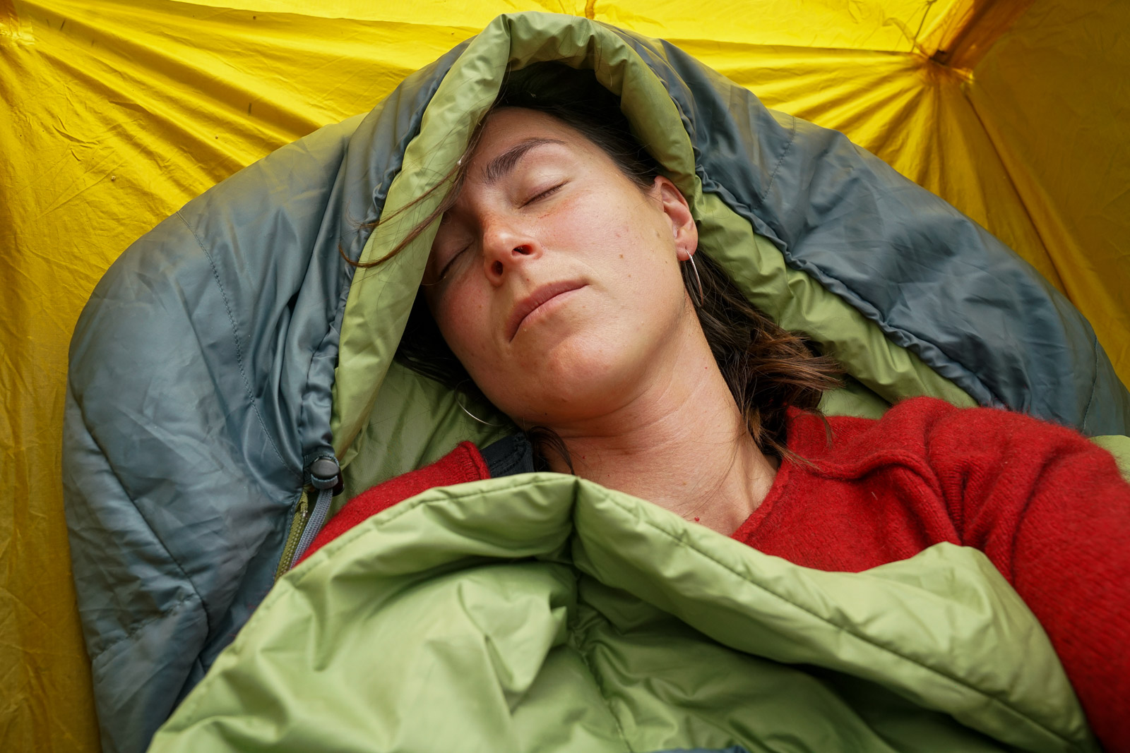 A close up of a sleeping person with their head in a sleeping bag hood.