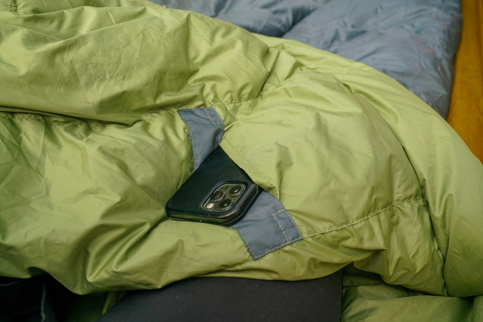 A close up of a smartphone sticking out of the pocket of a sleeping bag.