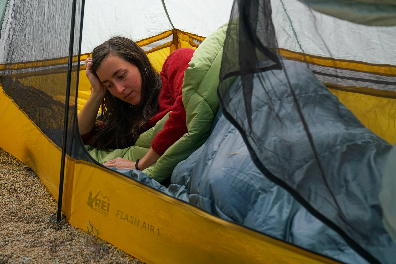 A person lays on their side in a sleeping bag inside a tent.