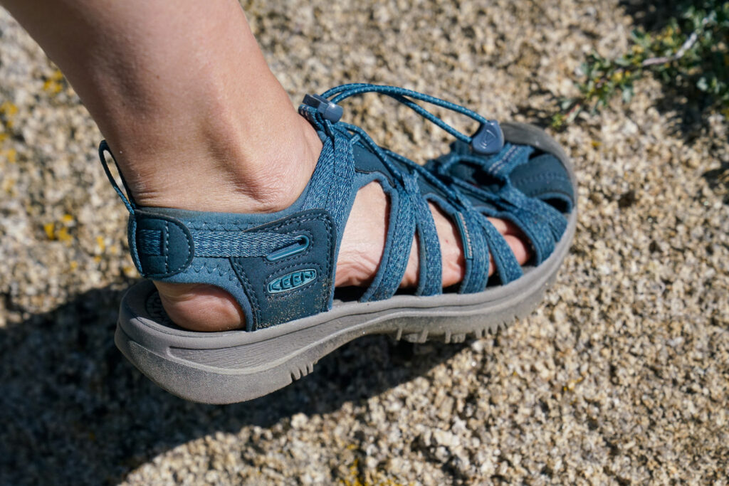 A close up of a single foot wearing a sandal standing on a rocky surface.